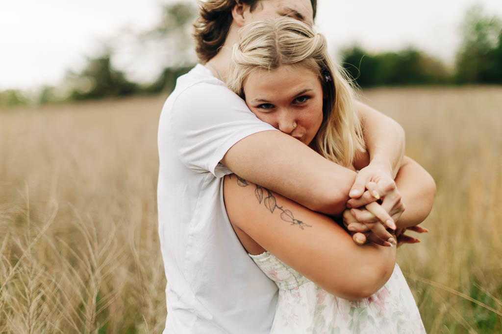 girl playfully kisses her boyfriend's arm while in his embrace in a grassy field near Harrison AR